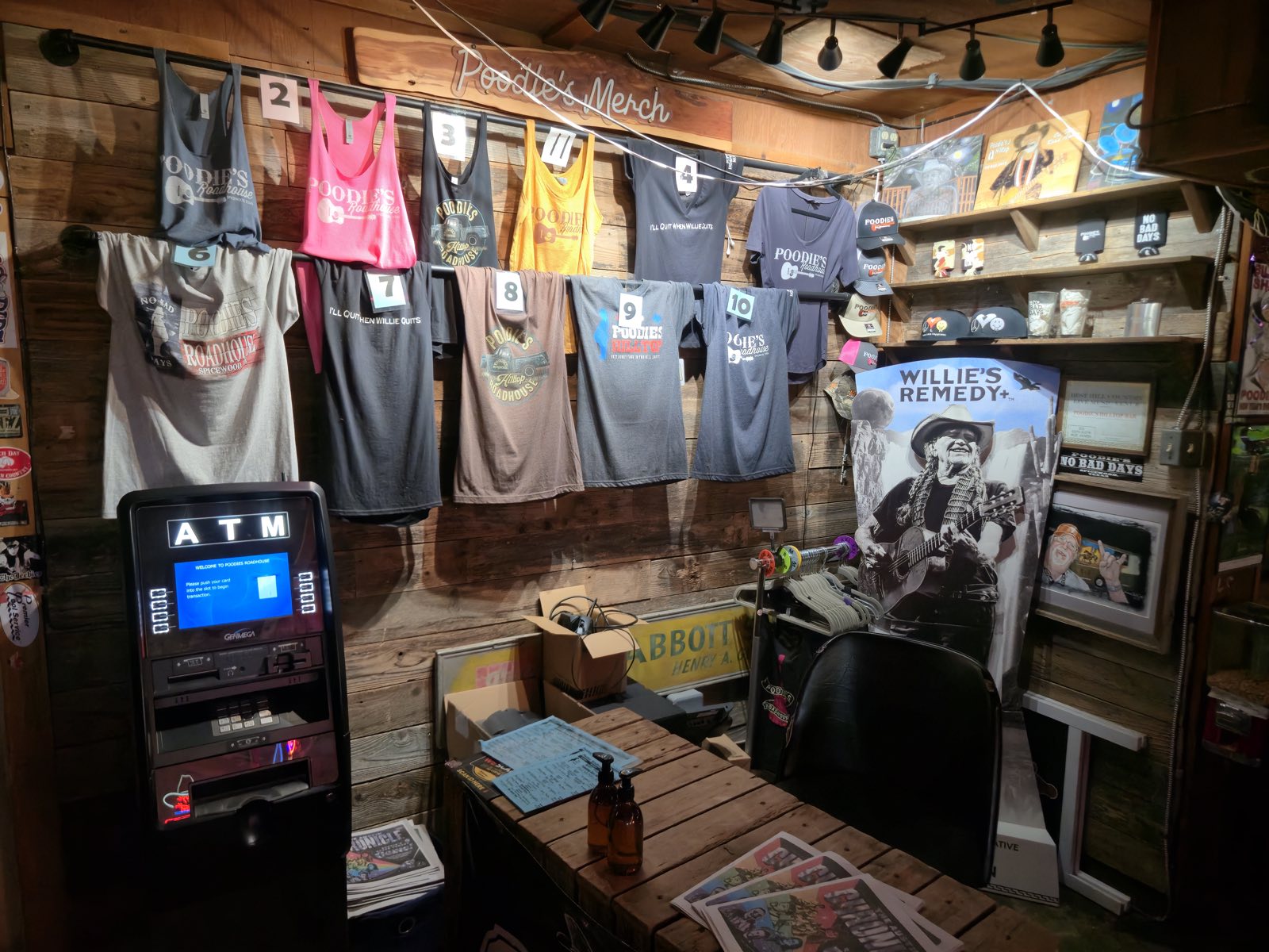 The Poodie's merch wall, hung with tees and tanks