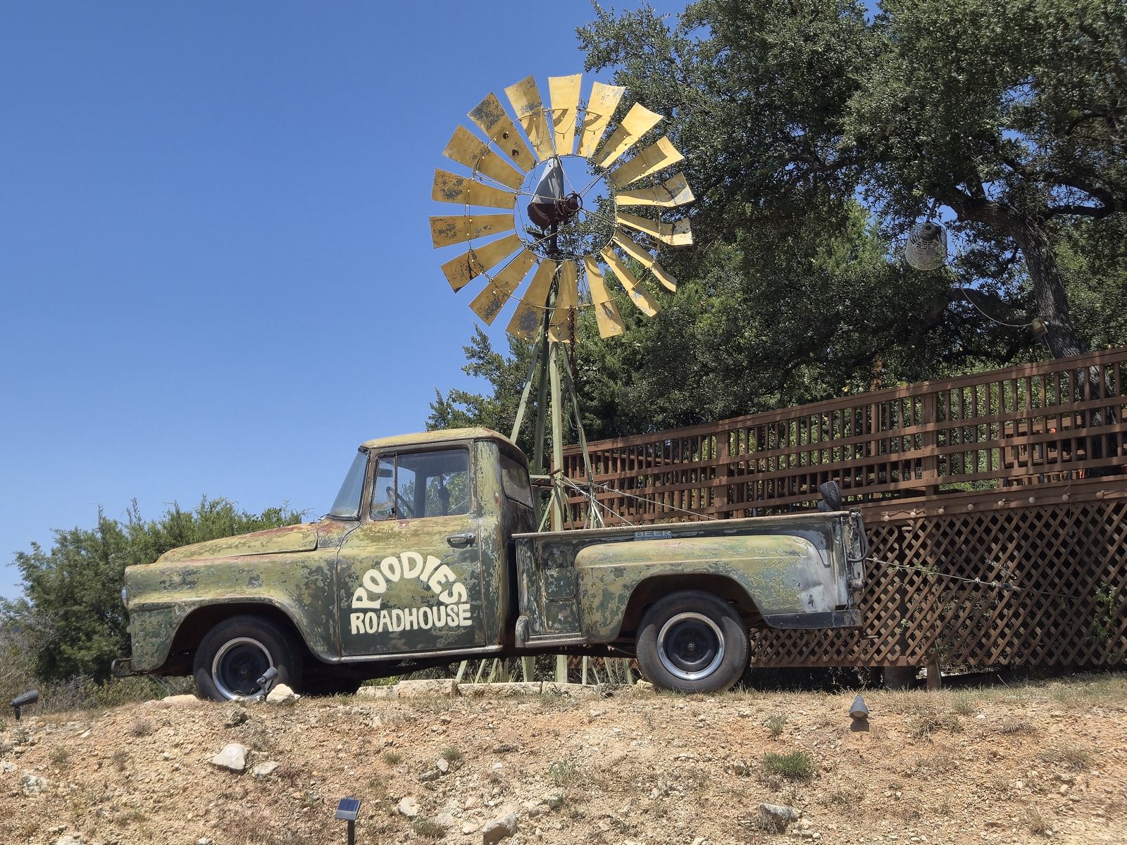 A vintage flatbed truck hand-painted POODIES ROADHOUSE, parked below the windmill on the hilltop at Poodie's
